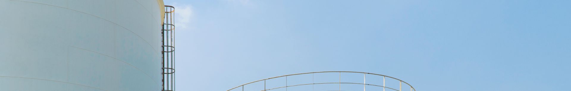 Large white cylindrical storage tanks with metal railings under a clear blue sky