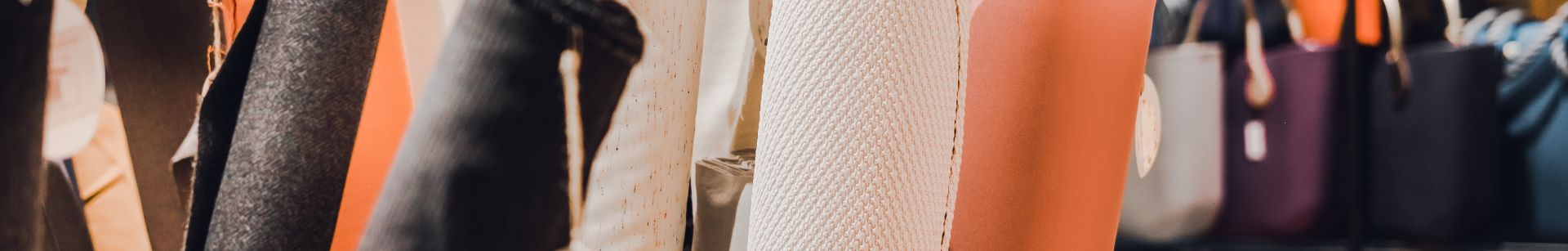 Rolls of fabric in various colors and textures displayed in a store, with shelves of bags and accessories in the background